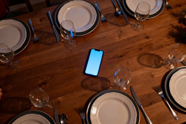 Table de repas de famille vue de dessus, assiettes et verres, un smartphone allume pose au centre.