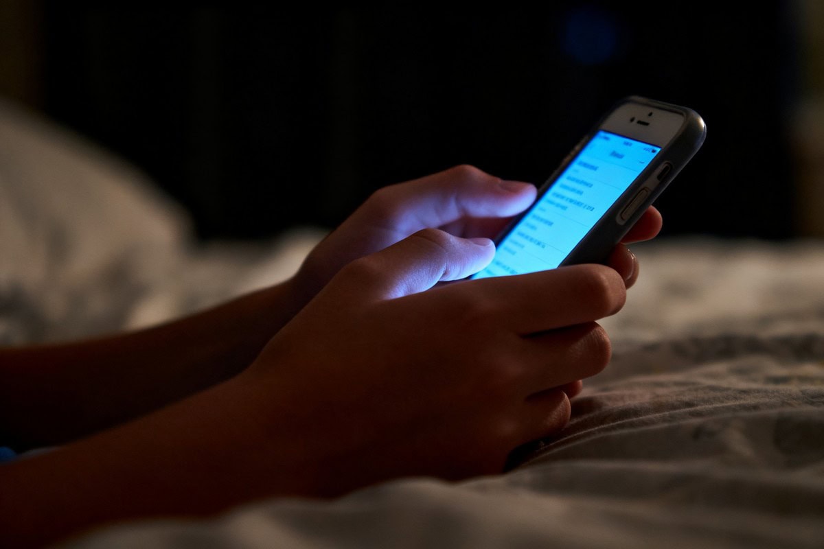 Mains d'adolescent tenant un smartphone allumé dans une chambre sombre la nuit.