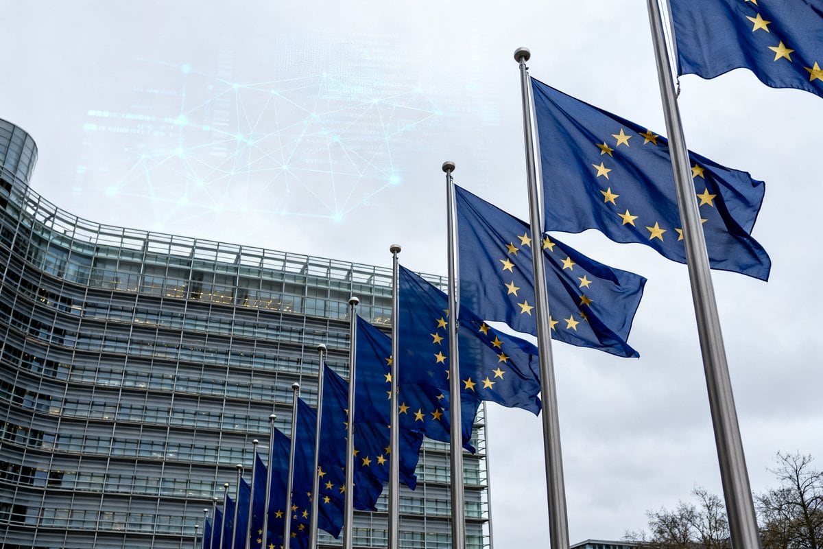 Rangée de drapeaux de l'Union européenne devant un bâtiment institutionnel vitré, sous un ciel gris