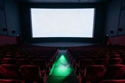 Salle de cinéma vide aux fauteuils rouges, écran blanc allumé et faisceau vert dans l'allée centrale