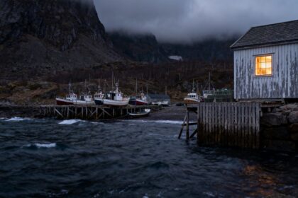 Village de pêcheurs au crépuscule, bateaux amarrés le long d'un quai en bois et fenêtre éclairée face à une mer agitée