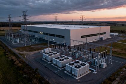 Grand centre de données sans fenêtres entouré de lignes à haute tension et d'unités de refroidissement au crépuscule
