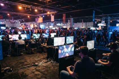 Joueurs assis manette en main devant des écrans dans une grande salle de salon de jeu vidéo bondée