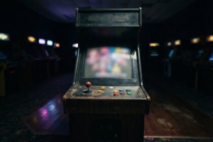 Borne d'arcade en bois usée au centre d'une salle sombre, écran allumé et boutons colorés sur le panneau de commande