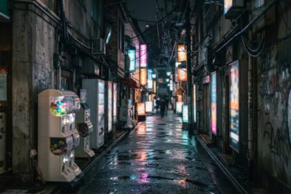 Ruelle nocturne bordée de panneaux lumineux flous et de distributeurs à capsules, asphalte mouillé