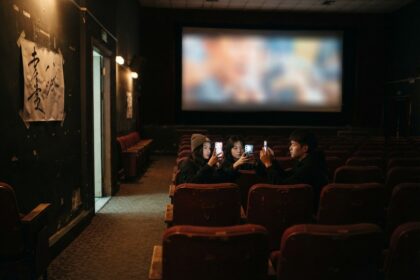 Trois spectateurs filment l'écran avec leur smartphone dans une salle de cinéma presque vide
