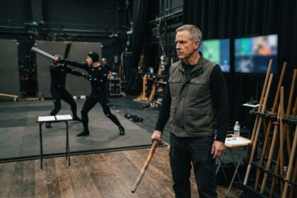 Un homme tient un sabre de bois dans un studio de captation de mouvement où deux performeurs s'affrontent