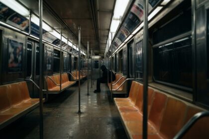 Rame de métro presque vide la nuit, une silhouette encapuchonnée assise seule sous les néons