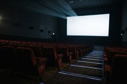 Salle de cinéma vide aux fauteuils rouges, l'écran blanc éclairé par un faisceau de projecteur