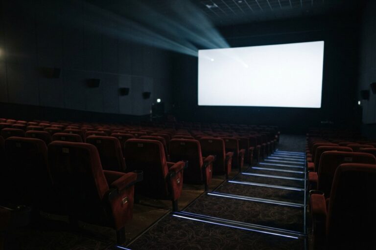 Salle de cinéma vide aux fauteuils rouges, l'écran blanc éclairé par un faisceau de projecteur