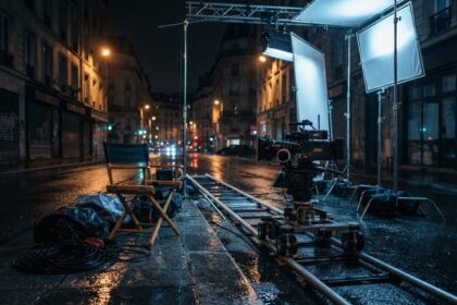 Plateau de tournage désert la nuit dans une rue mouillée, caméra sur rails, projecteurs et chaise de réalisateur.
