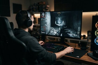 Joueur casqué de dos devant un écran PC affichant un jeu de tir à la première personne dans un couloir en ruine